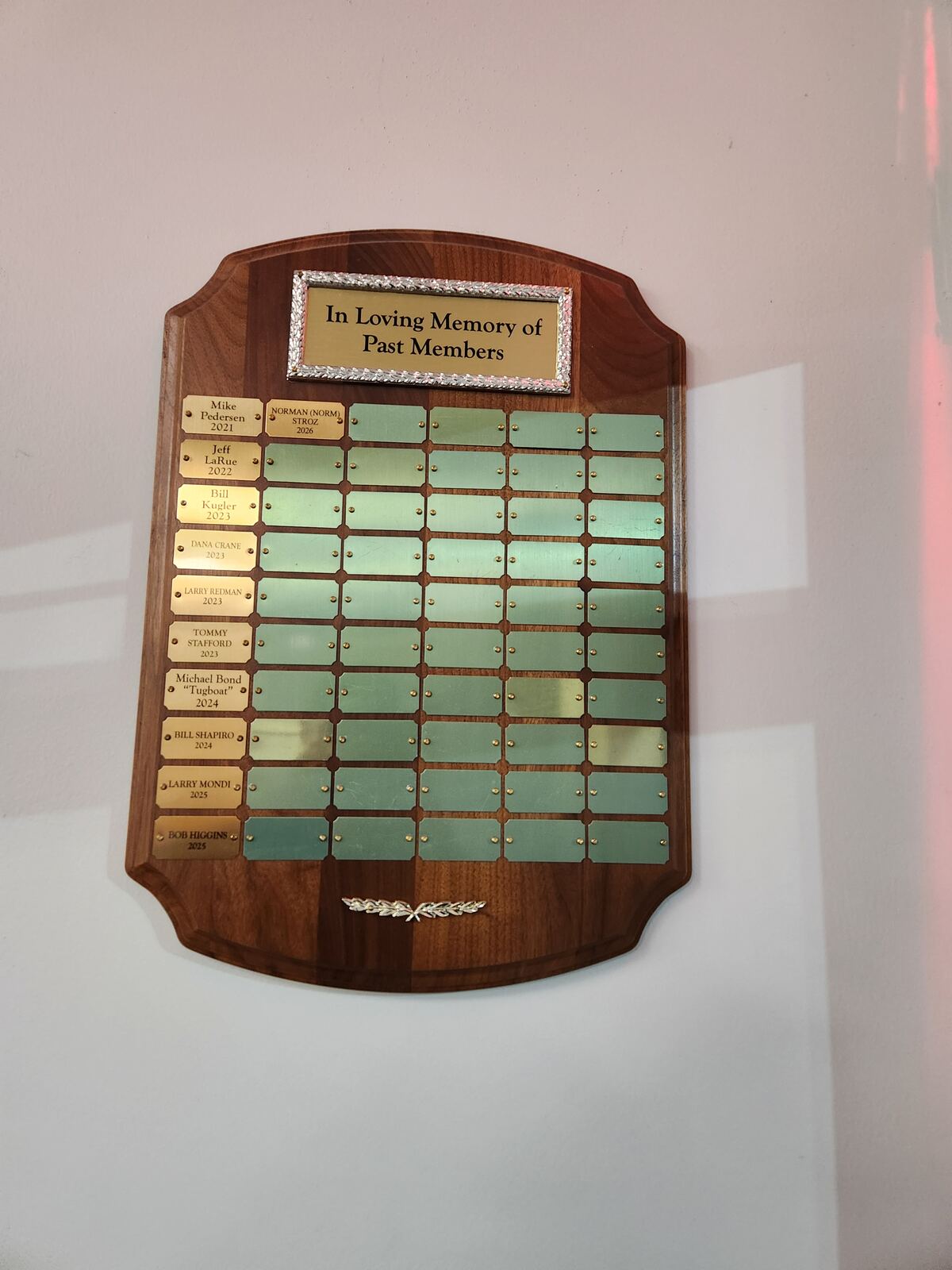A wooden memorial plaque with brass name plates, titled In Loving Memory of Past Members